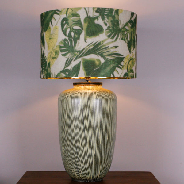 Die Lampe Botanical war ursprünglich eine Vase aus den 50er Jahren. Mit ihrem senkrecht verlaufenden Streifendesign in einem blassen Gelb und Grau, spiegelt die Vase die 50er Jahre wieder. Durch meine Idee, einen Deckel zu konstruieren, der die Gewindestange für den Lampenschirm als auch die Elektrik beinhaltet, kann die ehemalige Vase nun als Lampe erstrahlen. Der Lampenschirm ist mit seinem floralen Blattdesign sehr erfrischend. Für den kommenden Frühling ein Hingucker. Die goldenen Innenseite des Schirmes gibt ein schönes, warmes Licht ab.Die Lampe kann auch als Vase verwendet werden, da der Deckel nur in die Vase eingelassen ist. Wenn Sie eine kleine Wohnung haben und der Besuch bringt einen Blumenstrass mit, dann können Sie die Lampe zur Vase umfunktionieren.