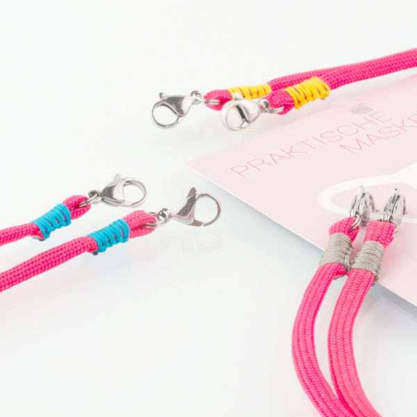 Das Masken Band ist der kleine Helfer im Alltag. Hier in der Farbkombi neon pink und sandgrau. Damit Du nicht ständig Deine Maske aus der Tasche holen musst, oder in der Hand hältst, hängst Du die Maske mit dem Band einfach um den Hals und steckst sie Dir in die Tasche Deines Oberhemdes, oder in die Revertasche Deiner Jacke, wenn Du sie nicht benötigst. Sie kann aber auch einfach runterhängen. Ob Du bei der Arbeit bist, in ein Geschäft, oder ins Restaurant gehst, Du kannst sie schnell aufsetzen. Sogar mit einer Hand ist das möglich. Die zwei Karabinerverschlüsse klemmst Du einfach an das Gummiband, das bei Gebrauch um die Ohren gelegt wird. Durch das Eigengewicht hängen die Karabiner an der tiefsten Stelle des Gummibandes, sodaß sie auch nicht an den Ohren drücken können. Die Maskenbänder werden mit Deinem Farbwunsch angefertigt. Wähle Deine Wunschfarbe für die Bänder, die die Karabiner halten, im Menü aus.