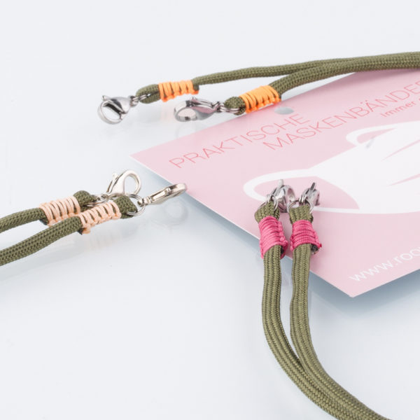 Das Maskenband ist der kleine Helfer im Alltag. Hier in der Farbkombi oliv und pink. Wer mutig ist, trägt Farbe. Damit Du nicht ständig Deine Maske aus der Tasche holen musst, oder in der Hand hältst, hängst Du die Maske mit dem Band einfach um den Hals und steckst sie Dir in die Tasche Deines Oberhemdes, oder in die Revertasche Deiner Jacke, wenn Du sie nicht benötigst. Sie kann aber auch einfach runterhängen. Ob Du bei der Arbeit bist, in ein Geschäft, oder ins Restaurant gehst, Du kannst sie schnell aufsetzen. Sogar mit einer Hand ist das möglich. Die zwei Karabinerverschlüsse klemmst Du einfach an das Gummiband, das bei Gebrauch um die Ohren gelegt wird. Durch das Eigengewicht hängen die Karabiner an der tiefsten Stelle des Gummibandes, sodaß sie auch nicht an den Ohren drücken können. Die Maskenbänder werden mit Deinem Farb-Wunsch angefertigt. Wähle Deine Wunschfarbe für die Bänder, die die Karabiner halten, im Menü aus.