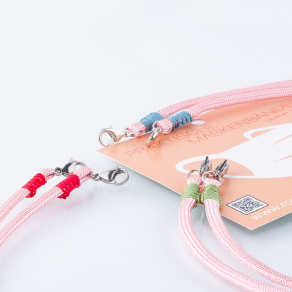 Das Maskenband ist der kleine Helfer im Alltag. Hier in einfarbig rosa. Damit Du nicht ständig Deine Maske aus der Tasche holen musst, oder in der Hand hältst, hängst Du die Maske mit dem Band einfach um den Hals und steckst sie Dir in die Tasche Deines Oberhemdes, oder in die Revertasche Deiner Jacke, wenn Du sie nicht benötigst. Sie kann aber auch einfach runterhängen. Ob Du bei der Arbeit bist, oder in ein Geschäft, oder ins Restaurant gehst, kannst Du sie schnell aufsetzen. Die zwei Karabinerverschlüsse klemmst Du einfach an das Gummiband, das bei Gebrauch um die Ohren gelegt wird. Durch das Eigengewicht hängen die Karabiner an der tiefsten Stelle des Gummibandes, sodaß sie auch nicht an den Ohren drücken können. Die Maskenbänder werden auf Deinen Farb-Wunsch hin angefertigt. Somit kannst Du Dir die Farbe der Bänder, die die Karabiner halten, im Menü aussuchen. Hier als Beispiel einmal drei Farbkombinationen.