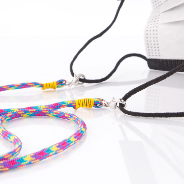 Das Maskenband ist der kleine Helfer im Alltag. Hier in der Farbkombi in Blau Pink Lila Gelb. Bunt ist für den Sommer immer perfekt. Sie passt sehr gut zu einer weissen Bluse, oder einem weissen Hemd. Damit Du nicht ständig Deine Maske aus der Tasche holen musst, oder in der Hand hältst, hängst Du die Maske mit dem Band einfach um den Hals und steckst sie Dir in die Tasche Deines Oberhemdes, oder in die Revertasche Deiner Jacke, wenn Du sie nicht benötigst. Sie kann aber auch einfach runterhängen. Ob Du bei der Arbeit bist, oder in ein Geschäft, oder ins Restaurant gehst, kannst Du sie schnell aufsetzen. Die zwei Karabinerverschlüsse klemmst Du einfach an das Gummiband, das bei Gebrauch um die Ohren gelegt wird. Durch das Eigengewicht hängen die Karabiner an der tiefsten Stelle des Gummibandes, sodaß sie auch nicht an den Ohren drücken können. Die Karabiner sind mit feinen Nylonbänder befestigt. Die Farben dieser Bänder kannst Du Dir über die Tabelle aussuchen. Die Maskenbänder werden dann daraufhin gefertigt. Stelle Dir Deine Farbkombi zusammen.