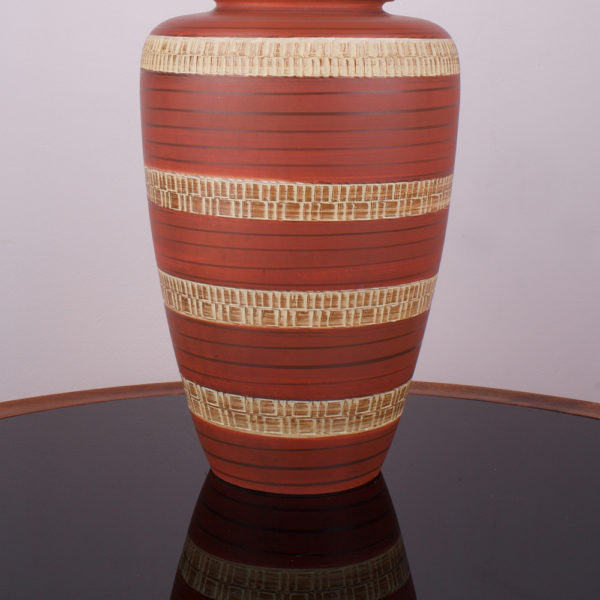 Die Tischlampe Bohemian in Terracotta Farbe hat eine warme Ausstrahlung. Die Farbe beruhigt und gibt dem Raum eine angenehme Atmosphäre. Der Lampenfuss besteht aus einer Vase aus den 1950er Jahren. Mittels einer Ritztechnik wurde in die Keramik ein geometrisches Muster in Ringen aufgebracht und anschließend wurde die Vase lasiert. Der Schirm und die Elektrik sind oben in den Hals der Vase eingesteckt und lassen sich bei Gebrauch der Vase abnehmen und auch als Blumenvase nutzen.