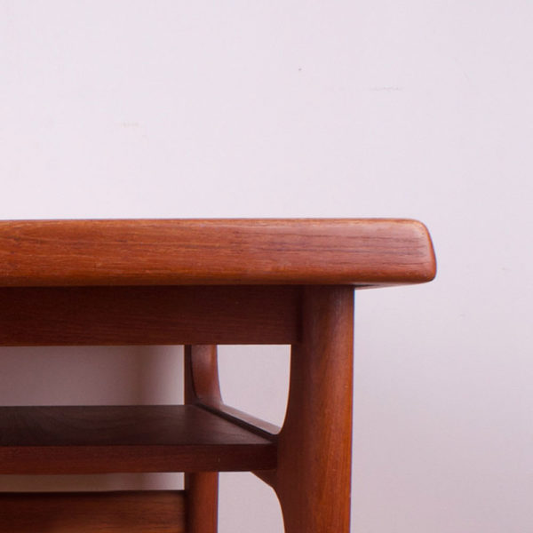 Der Designer Niels Bach hat für die Möbelmanufaktur Randers in den 1970er Jahren gestaltet. Der quadratische coffee table ist ein Designstück aus den 70er Jahren ist super praktisch für die kleine Wohnung. Der Tisch kann aber auch für ein großes Ecksofa, oder eine Wohnlandschaft genutzt werden. Der Tisch ist aus massivem Teakholz gefertigt. Eine unter der Hauptplatte angebrachte Zwischenplatte dient als praktische Zeitungsablage. Die Zwischenablage hat etwa eine Höhe von 10cm. Die Tischbeine ziehen sich in einer konisch verlaufenden Form von unten schmal nach oben etwas breiter werdend zu der unteren Platte. Auf den vier einsehbaren Seiten sind die Ecken zwischen den Beinen auf zwei Seiten abgerundet und auf den zwei anderen Seiten werden die Tischbeine durch jeweils eine Querstrebe gehalten und verstärkt.